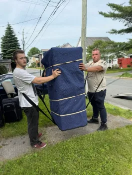 Deux déménageurs portent un meuble emballé de couverture bleue avec des sangles
